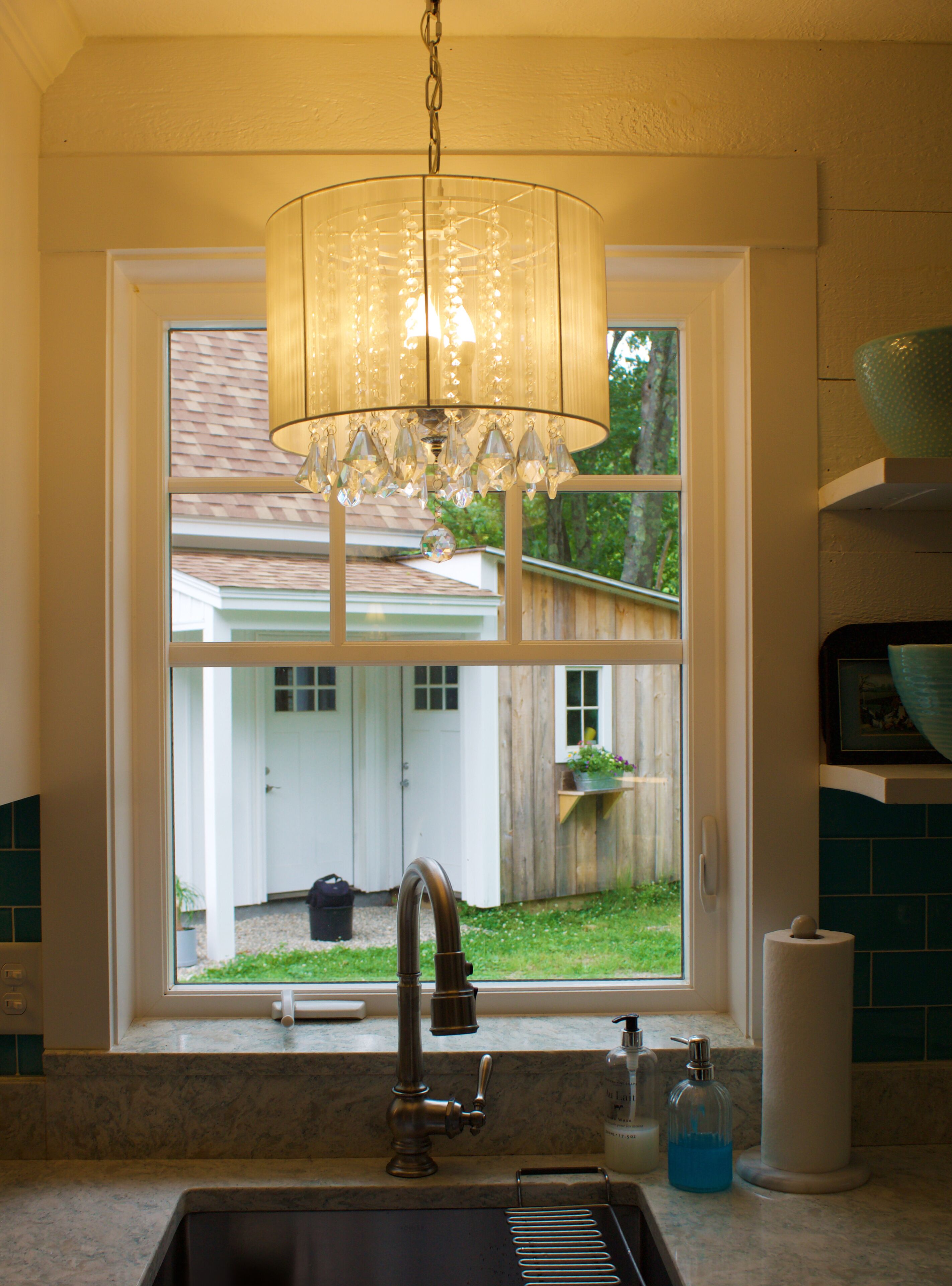 A kitchen with a sink, faucet, and a window overlooking a backyard.