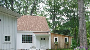 A house with a gravel driveway, a wooden deck, and a garden with flowers and plants. - Charming cottage apartment, private, quiet and sparkling clean.  1 bedrm 1 bath. (Kennebunk)