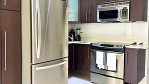A modern kitchen with stainless steel appliances, including a refrigerator, oven, and microwave, and dark wooden cabinets. - Modern 2BR Apartment Steps from La Concha & the Beach – Prime Condado (Santurce)