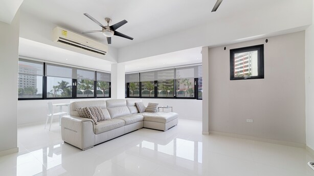 A spacious living room with a white sectional sofa, large windows, ceiling fans, and a tiled floor. - Modern 2BR Apartment Steps from La Concha & the Beach – Prime Condado (Santurce)