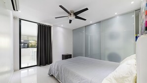 A modern bedroom with a bed, a ceiling fan, a sliding glass door, and a small bedside table. - Modern 2BR Apartment Steps from La Concha & the Beach – Prime Condado (Santurce)