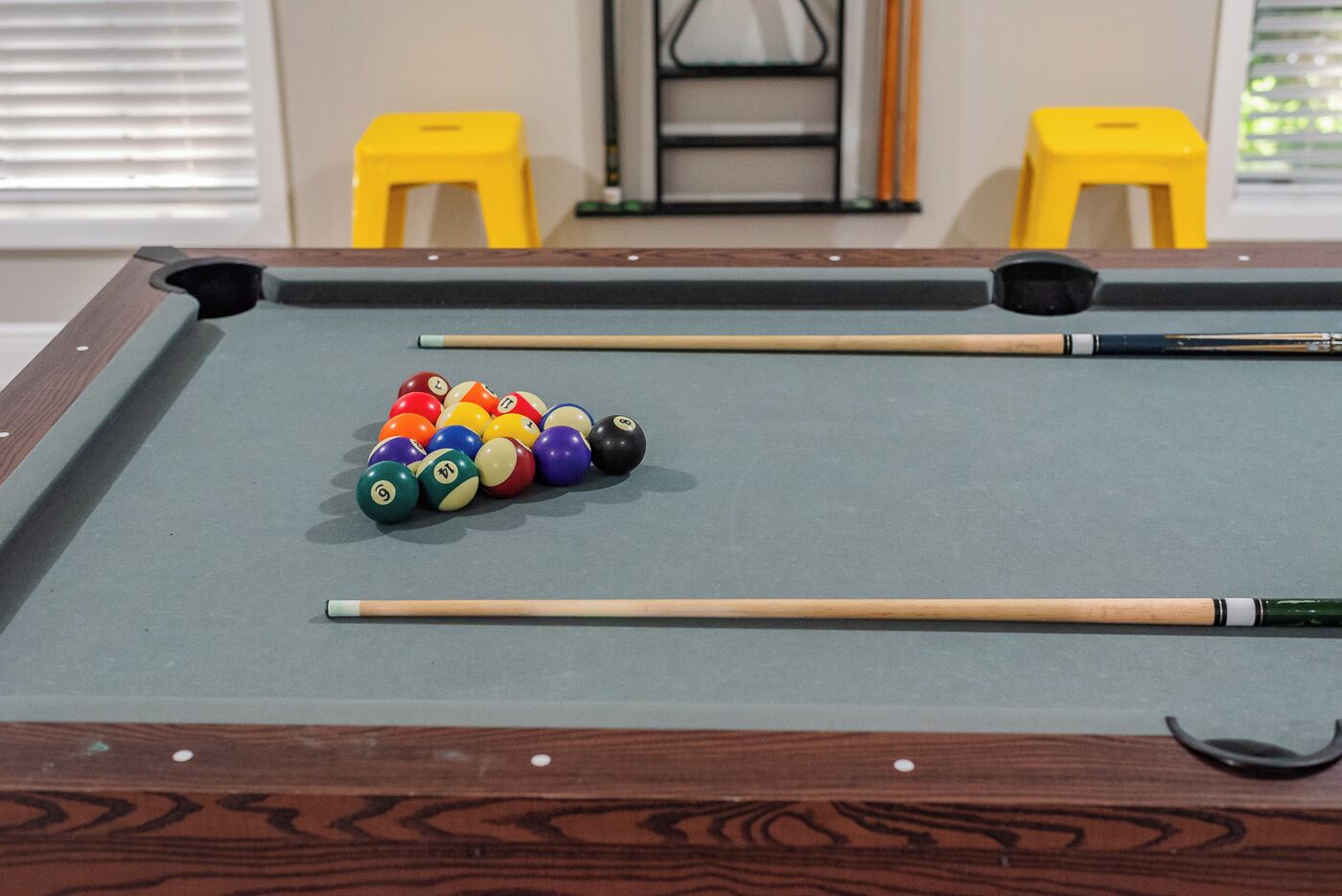 A pool table with colorful balls and two yellow stools in the background.