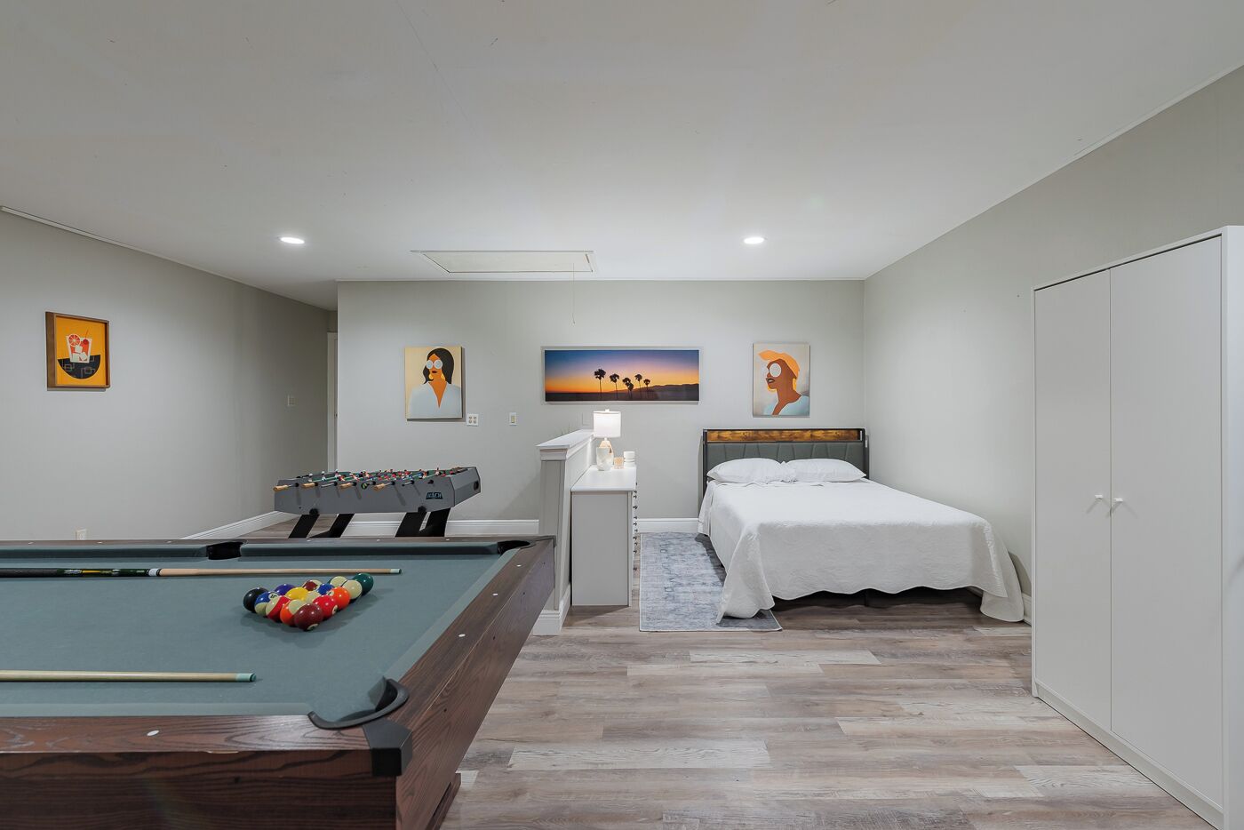 A bedroom with a pool table, a bed, and artwork on the walls.