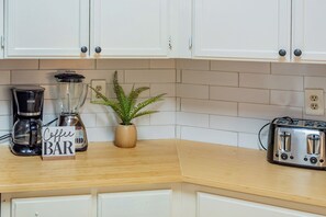 Una cocina con armarios blancos, cafetera, licuadora, tostadora y planta en maceta.