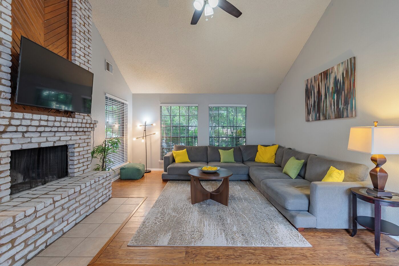 A living room with a fireplace, a grey sofa with yellow cushions, a coffee table, and a TV mounted on the wall.
