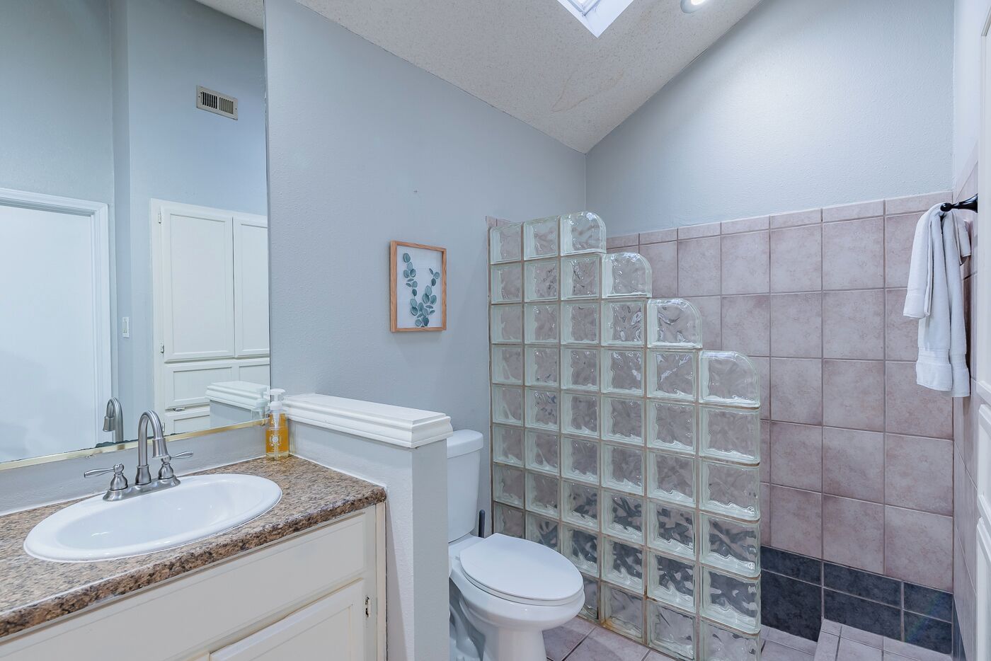 A bathroom with a granite countertop sink, a white toilet, and a glass shower enclosure.