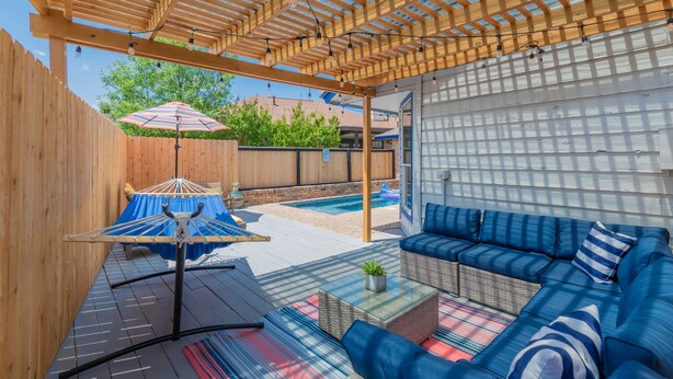 Un patio techado con una pérgola de madera, mobiliario exterior y una piscina.