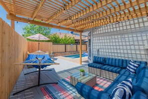 Un patio techado con una pérgola de madera, mobiliario exterior y una piscina.