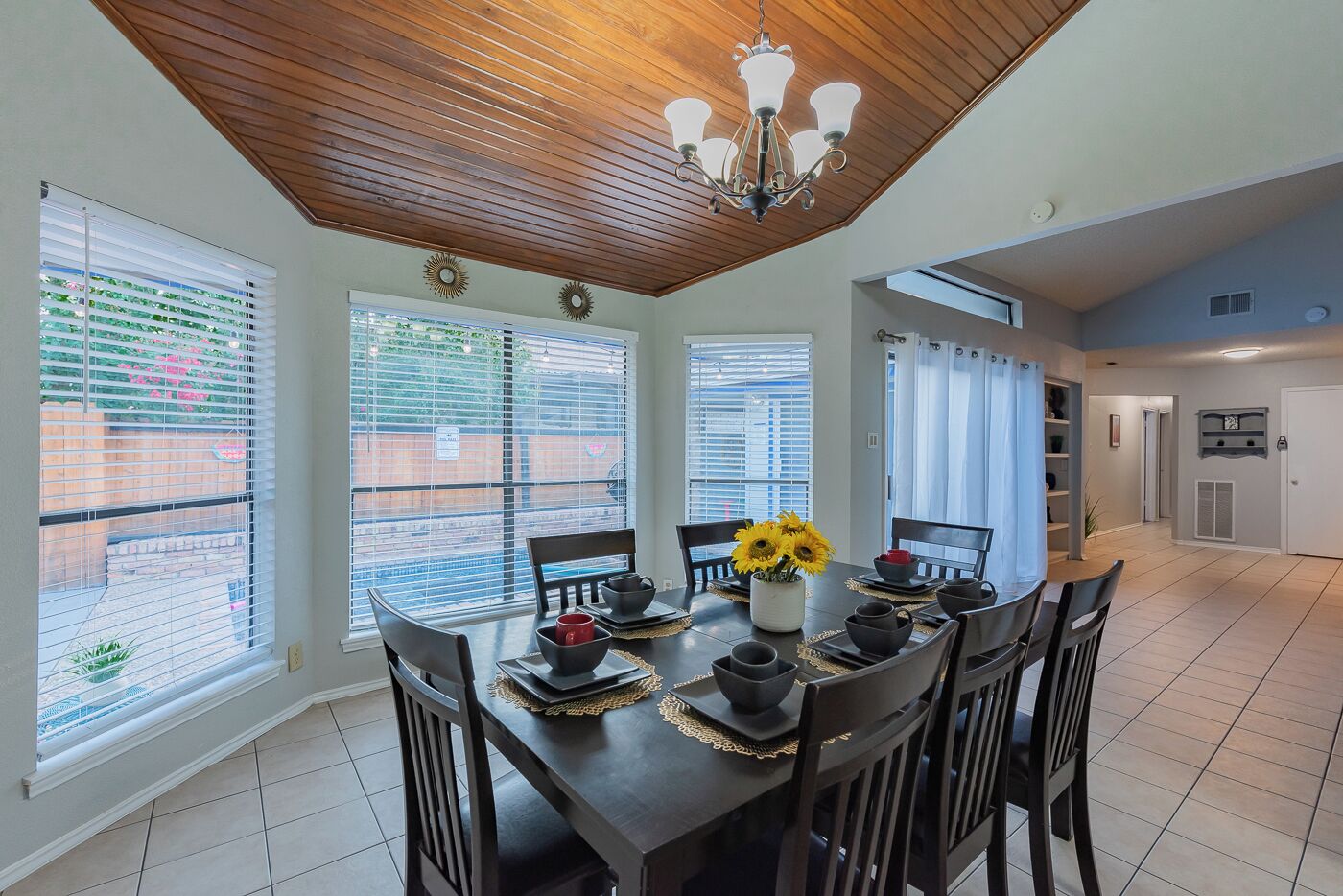 A dining area with a wooden ceiling, large windows, and a chandelier.