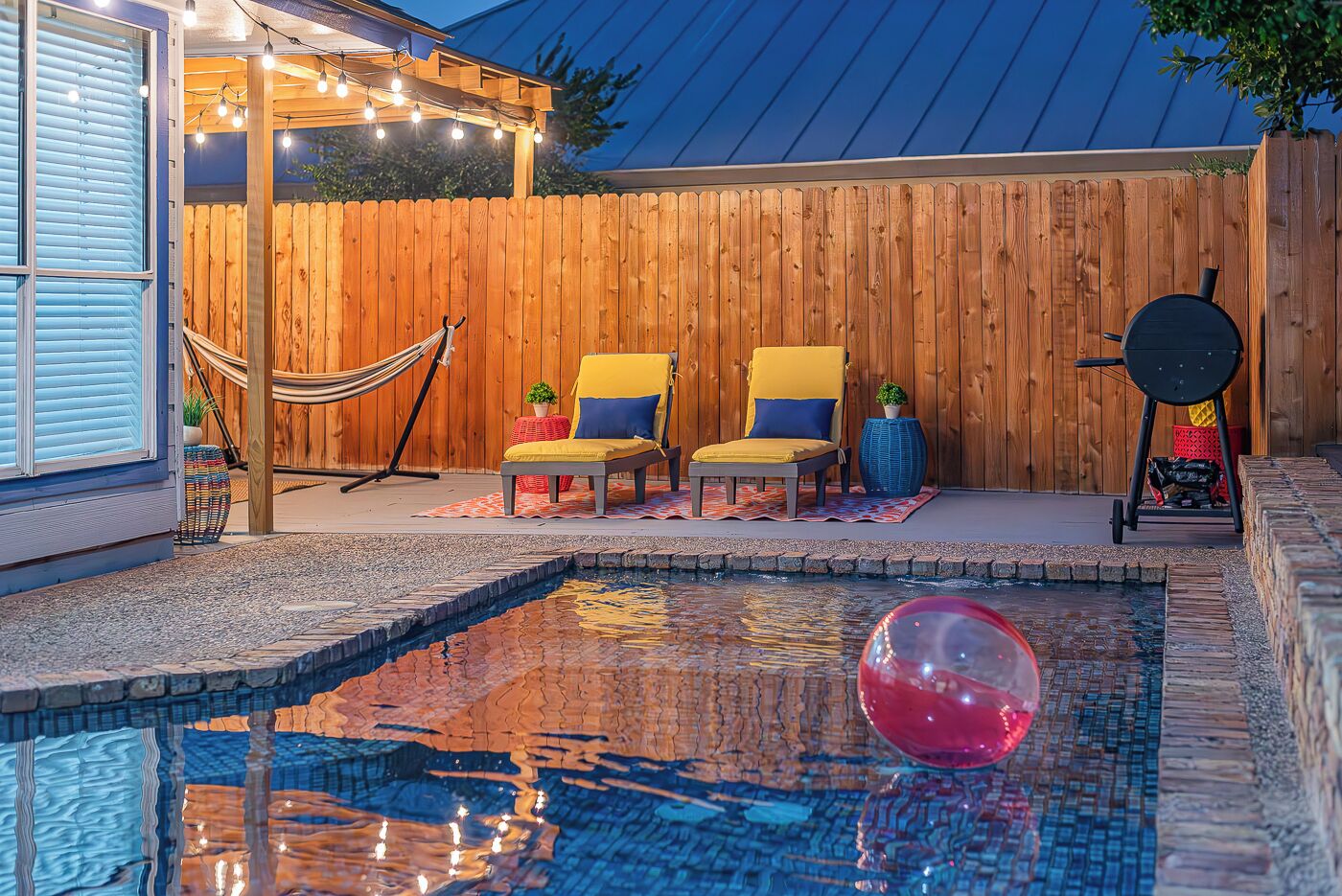 Ein Garten mit Swimmingpool, zwei gelben Stühlen, einer Hängematte und einem Grill.