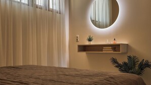 Une chambre à coucher avec un lit, un miroir rond, une étagère avec une plante et une fenêtre avec des rideaux.