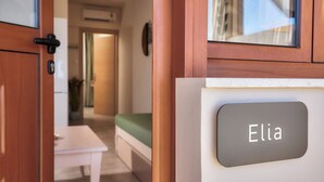 Une chambre avec un lit, une petite table et une plaque nominative portant le nom « Elia ».