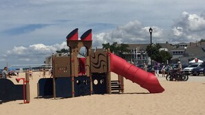 Un espace de jeux sur la plage avec un toboggan rouge et des structures d’escalade.