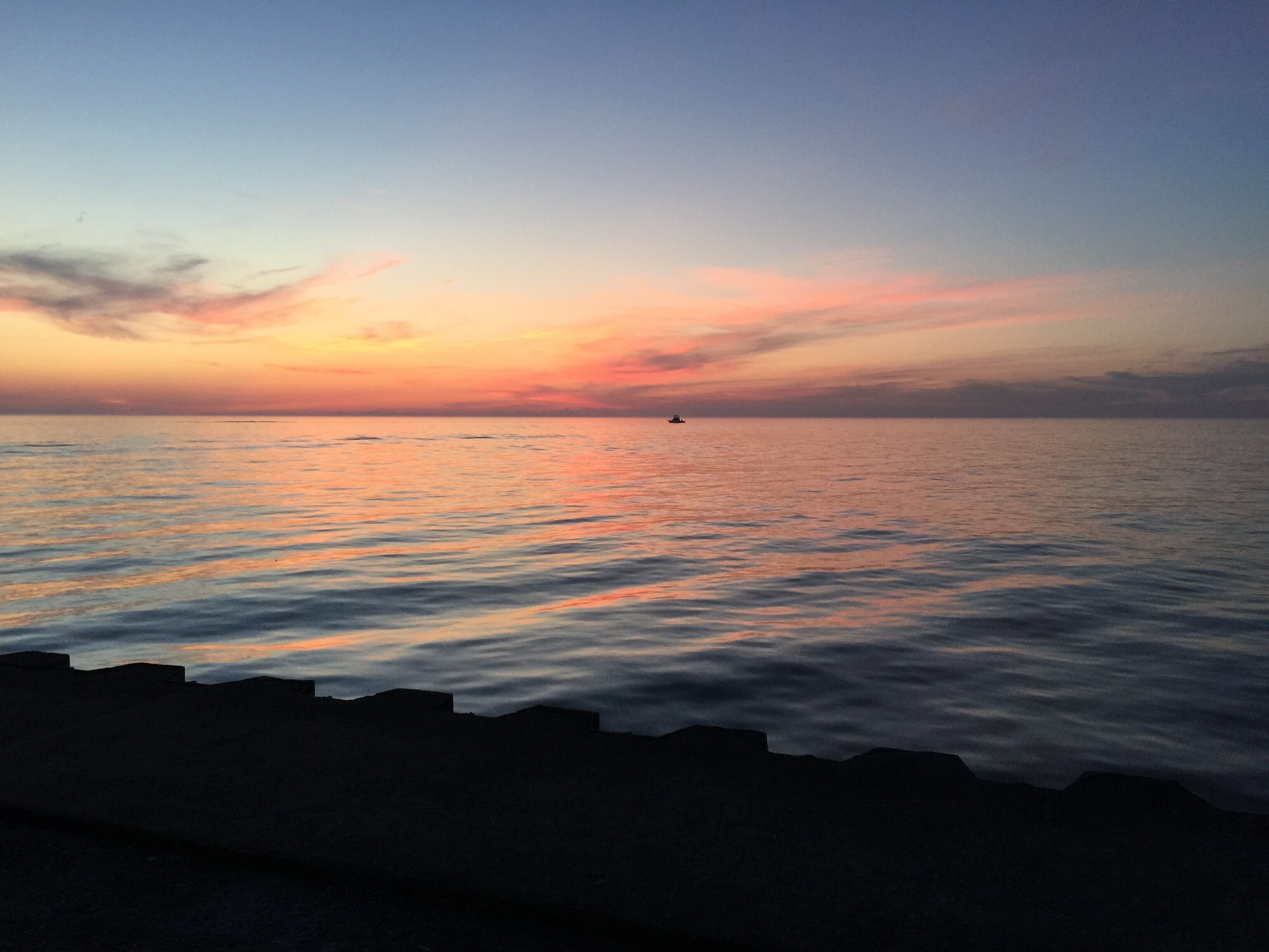 A calm sea at sunset with a silhouette of a boat in the distance.