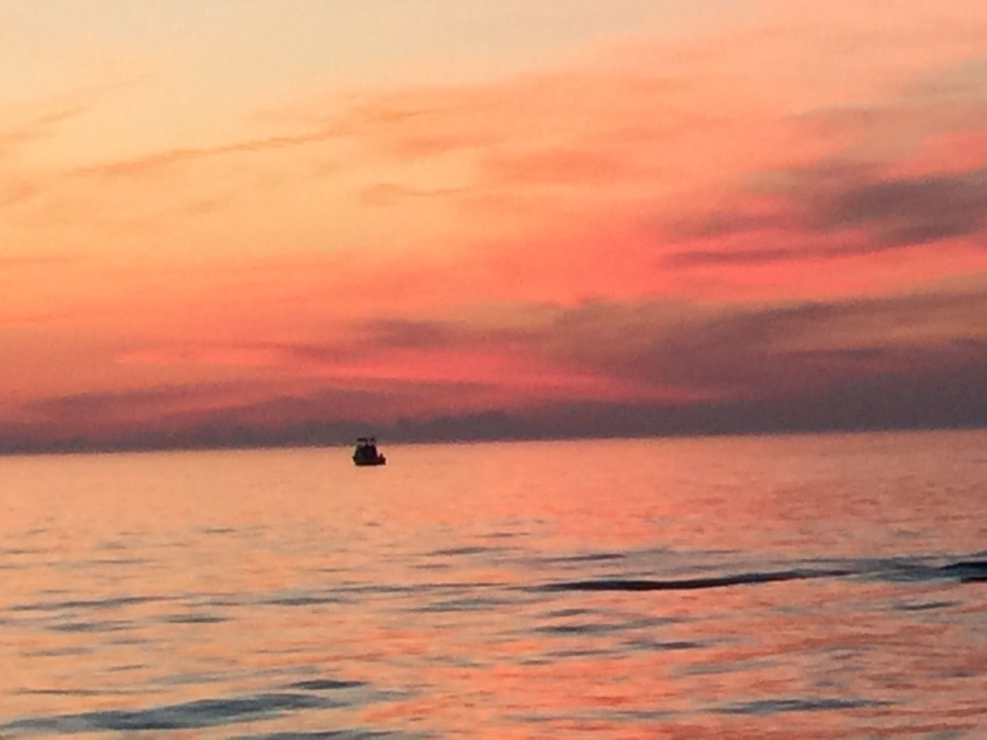 Un atardecer sobre un mar tranquilo con un barco pequeño a lo lejos.