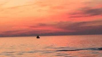 Un atardecer sobre un mar tranquilo con un barco pequeño a lo lejos.