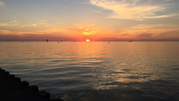 Un coucher de soleil sur une mer calme, avec des bateaux et un ciel dégagé.