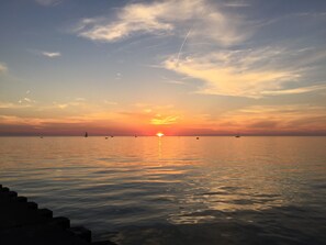 Ein Sonnenuntergang über einem ruhigen Meer mit Booten und wolkenlosem Himmel.