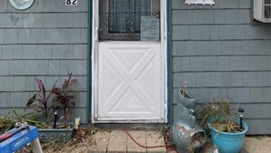 Une maison avec une porte blanche, le numéro 82, et un petit porche agrémenté d’une lanterne et de plantes en pot.