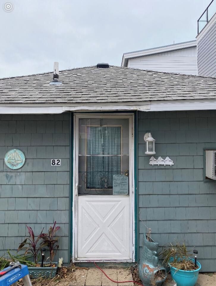 A house with a white door, number 82, and a small porch area with a lantern and potted plants.