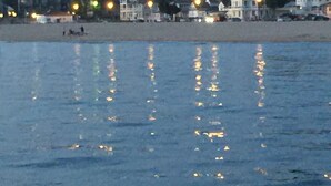 Une vue sur la plage, avec des maisons et une mer calme qui reflète les lumières.