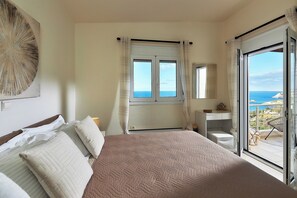 Une chambre avec un grand lit, une table de chevet, une chaise, une fenêtre avec des rideaux et une vue sur la mer.