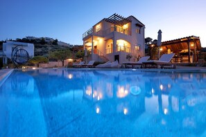 Un immeuble à plusieurs étages doté d’une piscine, de chaises longues et d’une pergola.