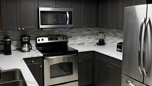 A modern kitchen with dark cabinetry, a stainless steel refrigerator, a microwave, a stove, and a coffee maker.