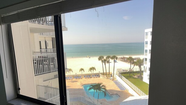 A view from a window overlooking a beach with a pool and lounge chairs.
