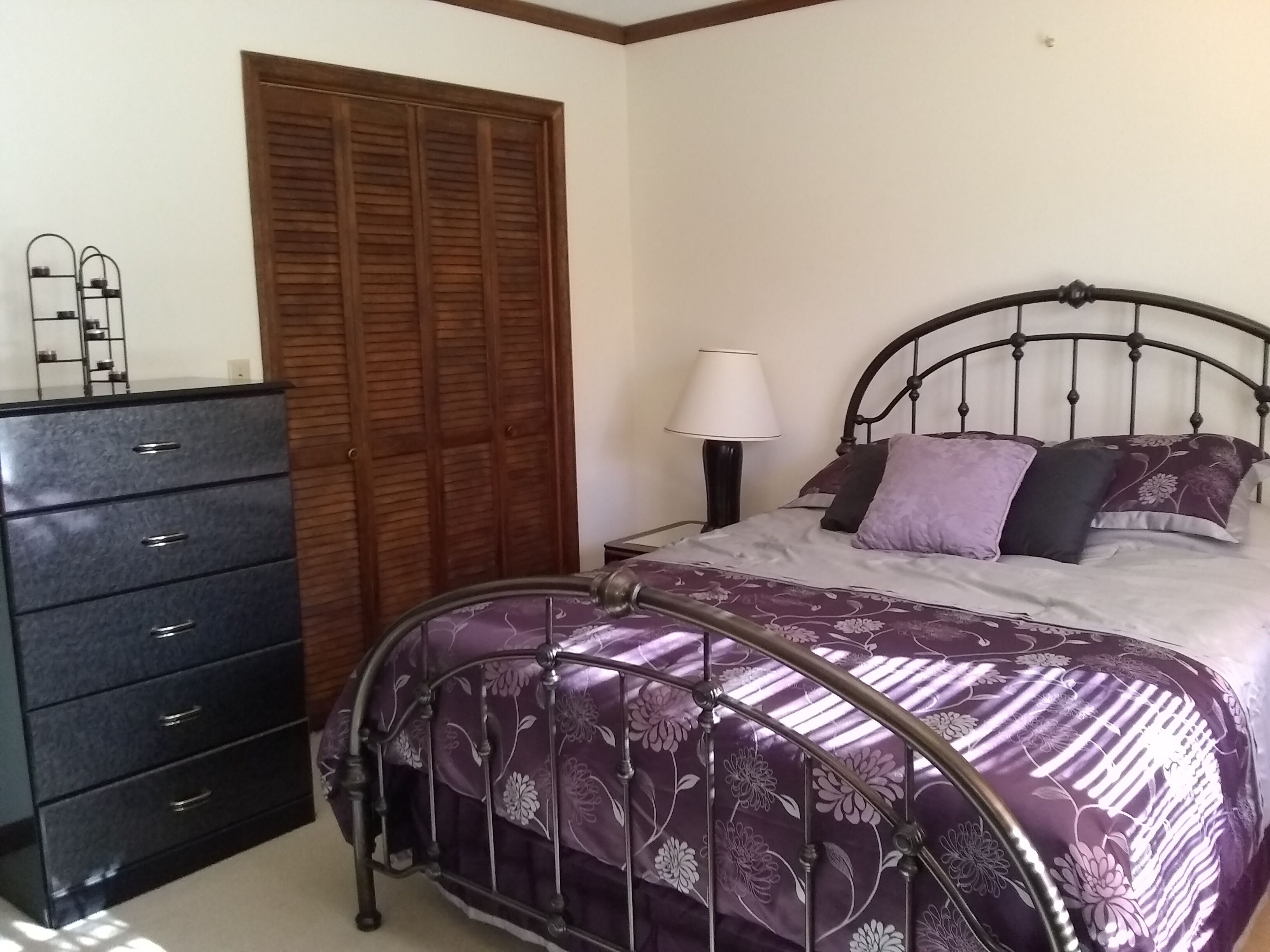Un dormitorio con cama, cómoda, lámpara y armario de madera.