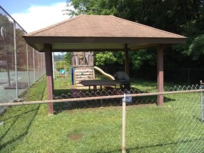 Un espacio exterior cercado con un pabellón de madera, una mesa de picnic y un parque infantil con tobogán.