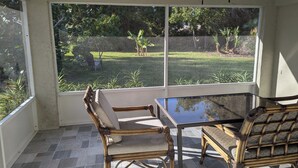 Ein Wintergarten mit Glastisch und zwei Korbstühlen, großen Fenstern und einem Deckenventilator.
