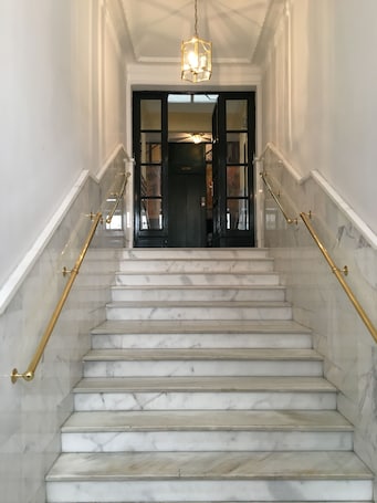 A marble staircase with gold handrails leading to a dark door with glass panels.