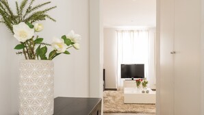 Un salon moderne avec un téléviseur, une table basse blanche et un vase décoratif rempli de fleurs.