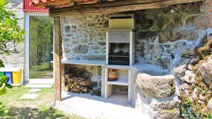 A stone building with a wooden roof, a glass door, and a small outdoor area with a fire pit and logs. - Villa with private pool near Gerês (Terras de Bouro)