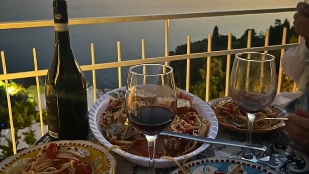 A table with plates of pasta and wine glasses, overlooking a body of water at sunset. - Casa Rosetta: A terrace on the sea paradise of the Amalfi Coast (Praiano)