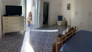 A bedroom with a bed, a TV on a dresser, a chair, a wardrobe, and a potted plant. - Casa Rosetta: A terrace on the sea paradise of the Amalfi Coast (Praiano)