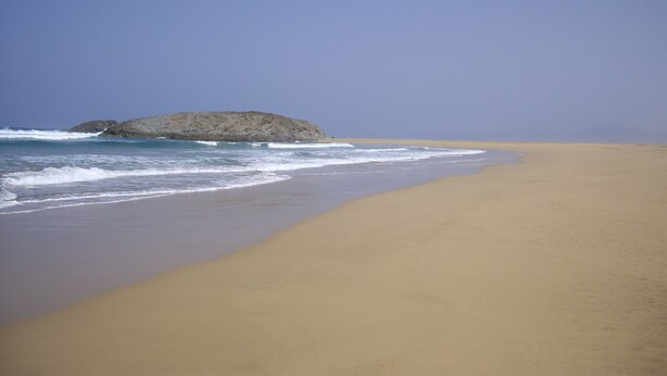 A wide sandy beach with gentle waves and a rocky outcrop in the distance. - Morisca Lapiada House (Morro Jable)