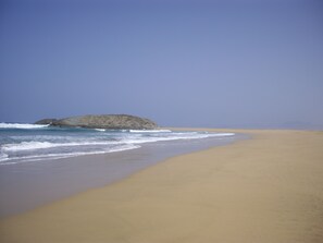 A wide sandy beach with gentle waves and a rocky outcrop in the distance. - Morisca Lapiada House (Morro Jable)