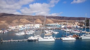 A marina with multiple boats docked, a small town in the background, and a clear sky. - Morisca Lapiada House (Morro Jable)