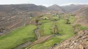 A golf course with a view of a mountainous landscape and a building in the distance. - Morisca Lapiada House (Morro Jable)