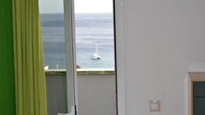 A room with a view of the sea through a window, a green curtain, and a white wall with a light switch. - Morisca Lapiada House (Morro Jable)
