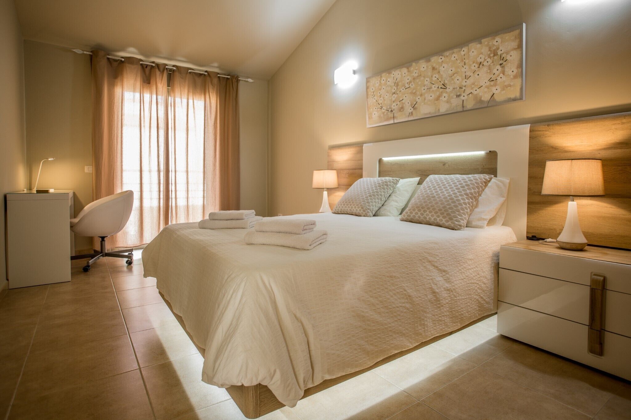 Ein ordentlich eingerichtetes Schlafzimmer mit einem großen Bett, Nachttischlampen, einem Schreibtisch und einem Stuhl.
