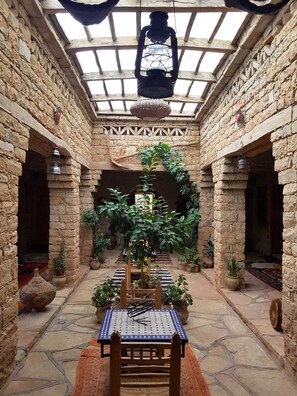 Un patio central con una mesa y sillas, rodeado de muros de piedra y plantas en macetas.