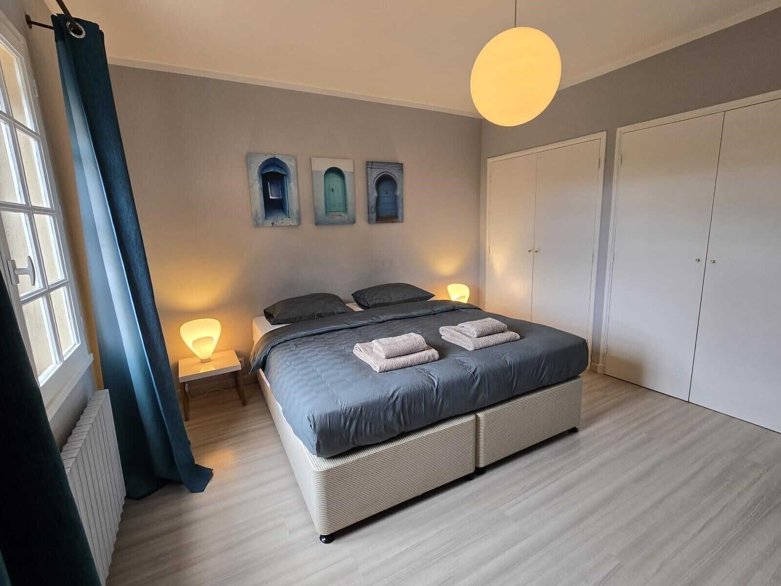 A bedroom with a bed, bedside lamps, a window with curtains, and a wardrobe.