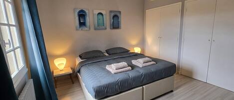 A bedroom with a bed, bedside lamps, a window with curtains, and a wardrobe.