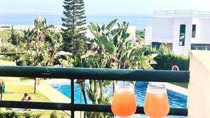 Un balcón con vista a la piscina, dos bebidas y un cuenco de frutos secos.