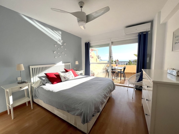 Une chambre à coucher comprenant un lit, des tables de chevet, un bureau, une chaise et un balcon avec vue.
