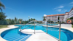A swimming pool with a curved design, surrounded by a fence, and a building with balconies in the background. - Manilva Andalusië, Spain (Manilva)