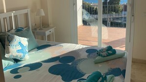 A bedroom with a bed, a nightstand, a lamp, and a view of the sea through a sliding door. - Manilva Andalusië, Spain (Manilva)